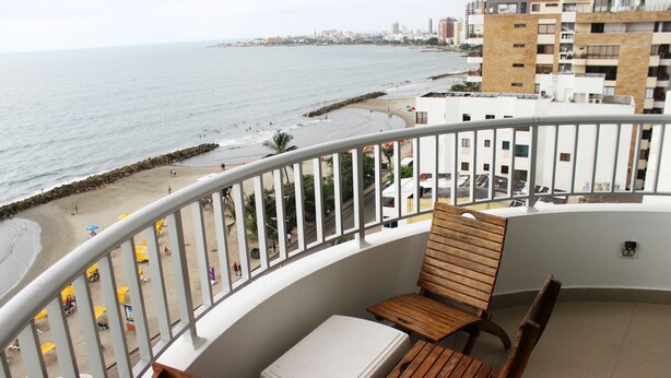 Een balkon met uitzicht op het strand, een tafel en twee houten stoelen.