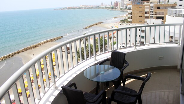 Ein Balkon mit Glastisch und Stühlen mit Blick auf Strand und Stadtpanorama.