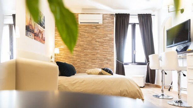 Quarto de hotel moderno com cama, escrivaninha e cadeira, televisão e janela com cortinas.