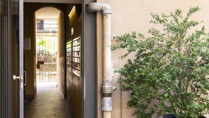 Um corredor com piso ladrilhado, uma planta em vaso e um cano de utilidades.