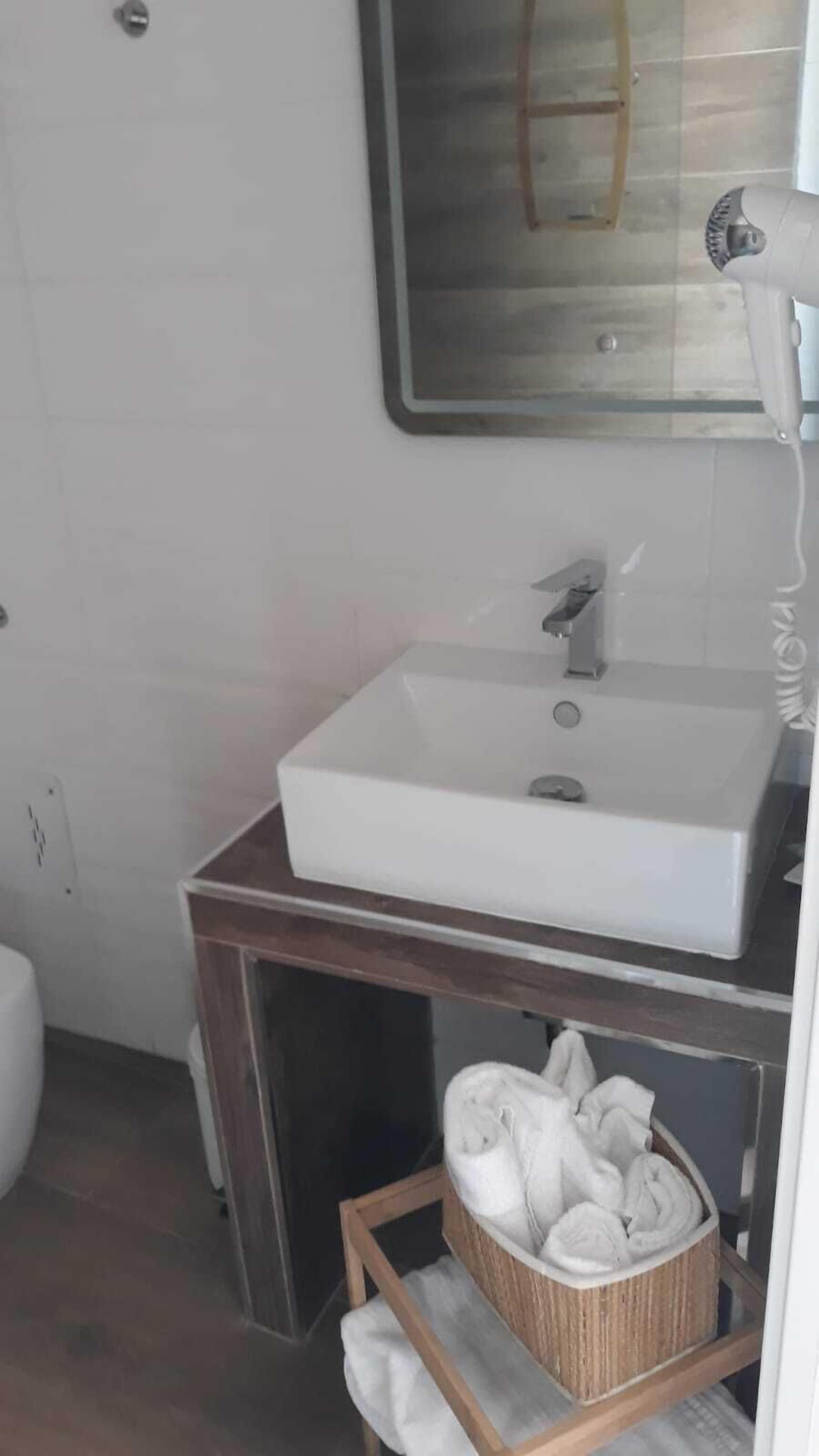 Un baño con lavamanos blanco, tocador de madera, espejo y toallero con toallas.