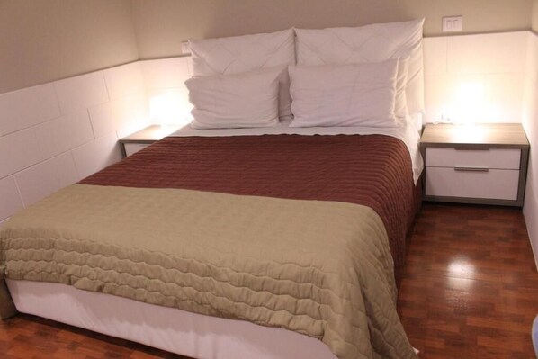 Un lit bien fait, recouvert d’une couverture marron et blanche, deux tables de chevet avec des lampes et un plancher en bois.