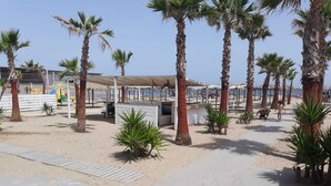A beachside area with palm trees, a covered seating area, and a small kiosk. - Gazebo Rooms (Margherita di Savoia)