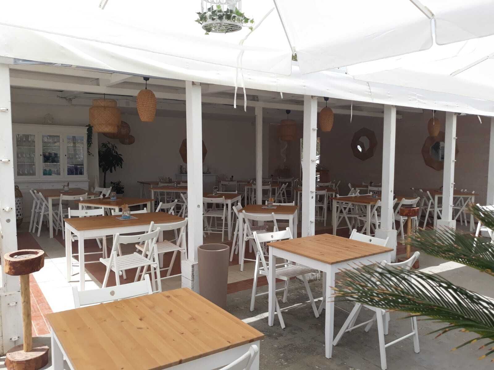 An outdoor cafe with white tables and chairs, hanging wicker lamps, and a white canopy.