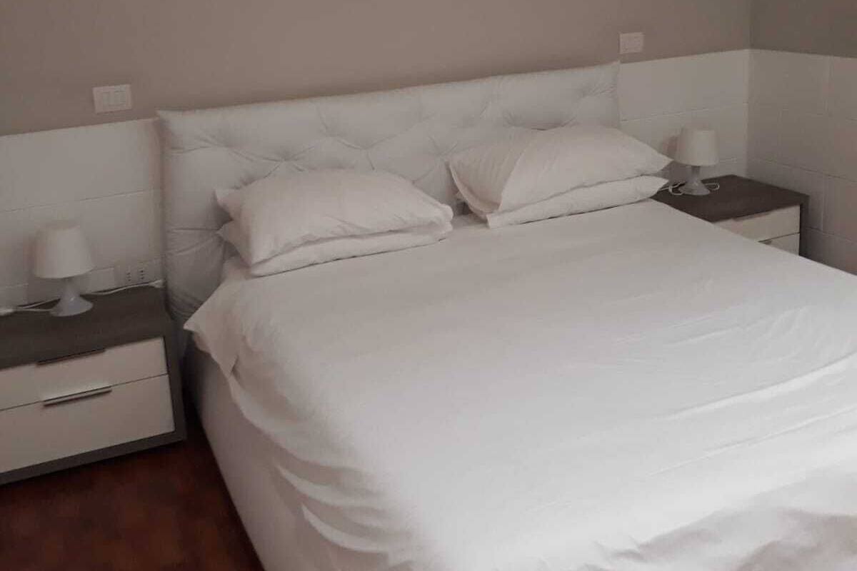 Una cama bien hecha con ropa blanca en una habitación de diseño sencillo y limpio.