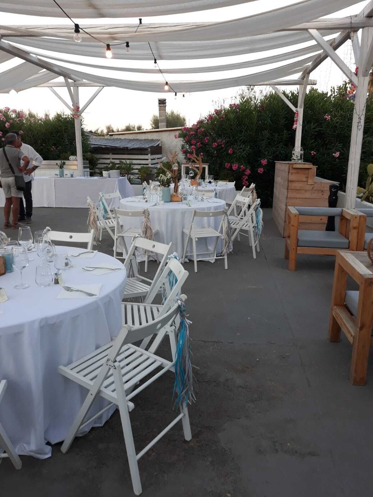 An outdoor dining area with round tables covered with white tablecloths, white chairs, and string lights.