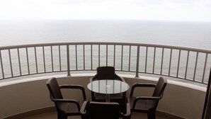 Un balcon avec une table en verre et quatre chaises, donnant sur une mer calme.