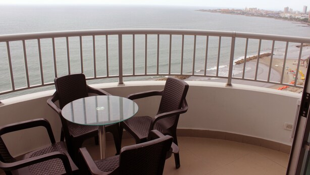 Un balcon avec une table et des chaises en verre, donnant sur une plage et la mer.