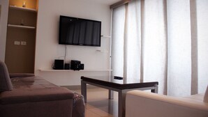 Un salon moderne avec un téléviseur à écran plat fixé au mur, un canapé, une table basse et une fenêtre avec des rideaux.