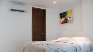 Une chambre à coucher avec un lit, une porte, un appareil de climatisation et un tableau au mur.