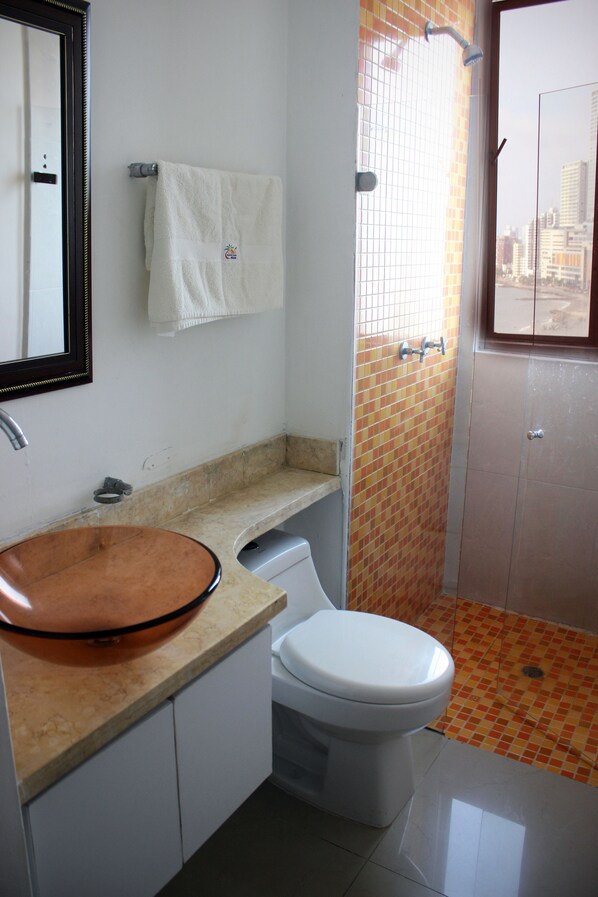 Un baño con inodoro blanco, lavamanos marrón, espejo y ducha con paredes de azulejos naranjas.