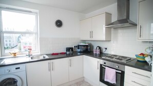 Une cuisine moderne avec des meubles blancs, une hotte en acier inoxydable, un four à micro-ondes et un lave-linge.