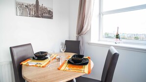 Une table à manger dressée avec des assiettes, des couverts et un verre à vin, avec une vue sur le paysage urbain par la fenêtre.