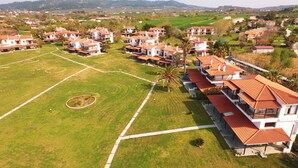 Un barrio residencial con varias casas de dos pisos, techos de tejas rojas y paredes blancas, rodeado de céspedes verdes y algunas palmeras.