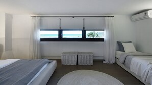 Un dormitorio con cama, ventana con vista al mar, una mesita y una mesita de noche.