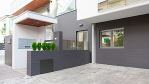 A modern building with a grey facade, a wooden slatted roof, and a small garden area with trimmed bushes. - Le Mie Città (Pescara)