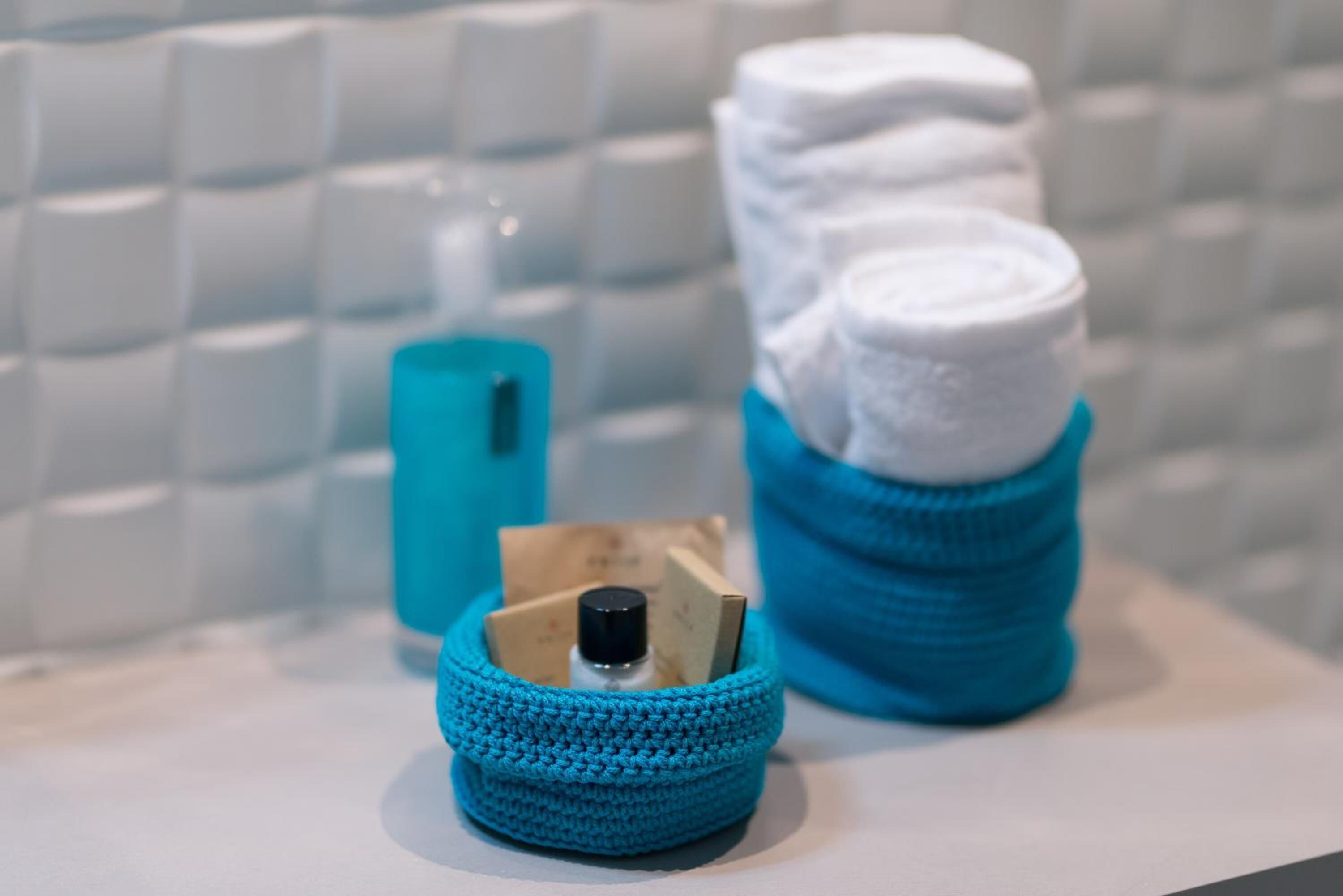 A bathroom with a white tiled wall, a blue towel holder with folded towels, and a blue bottle.