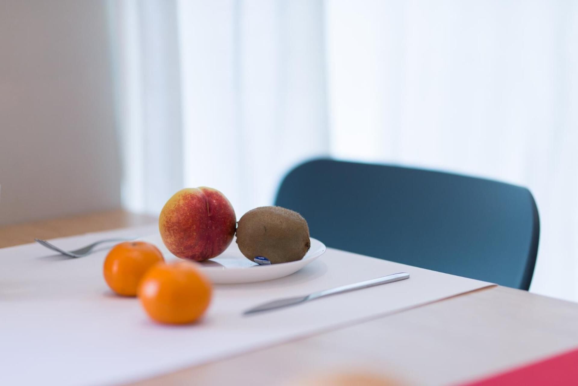 A dining table with a plate of fruit, including a peach and a kiwi, and two small oranges.