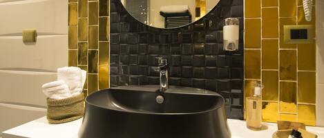 A bathroom with a black sink, a round mirror, and a yellow-tiled wall.