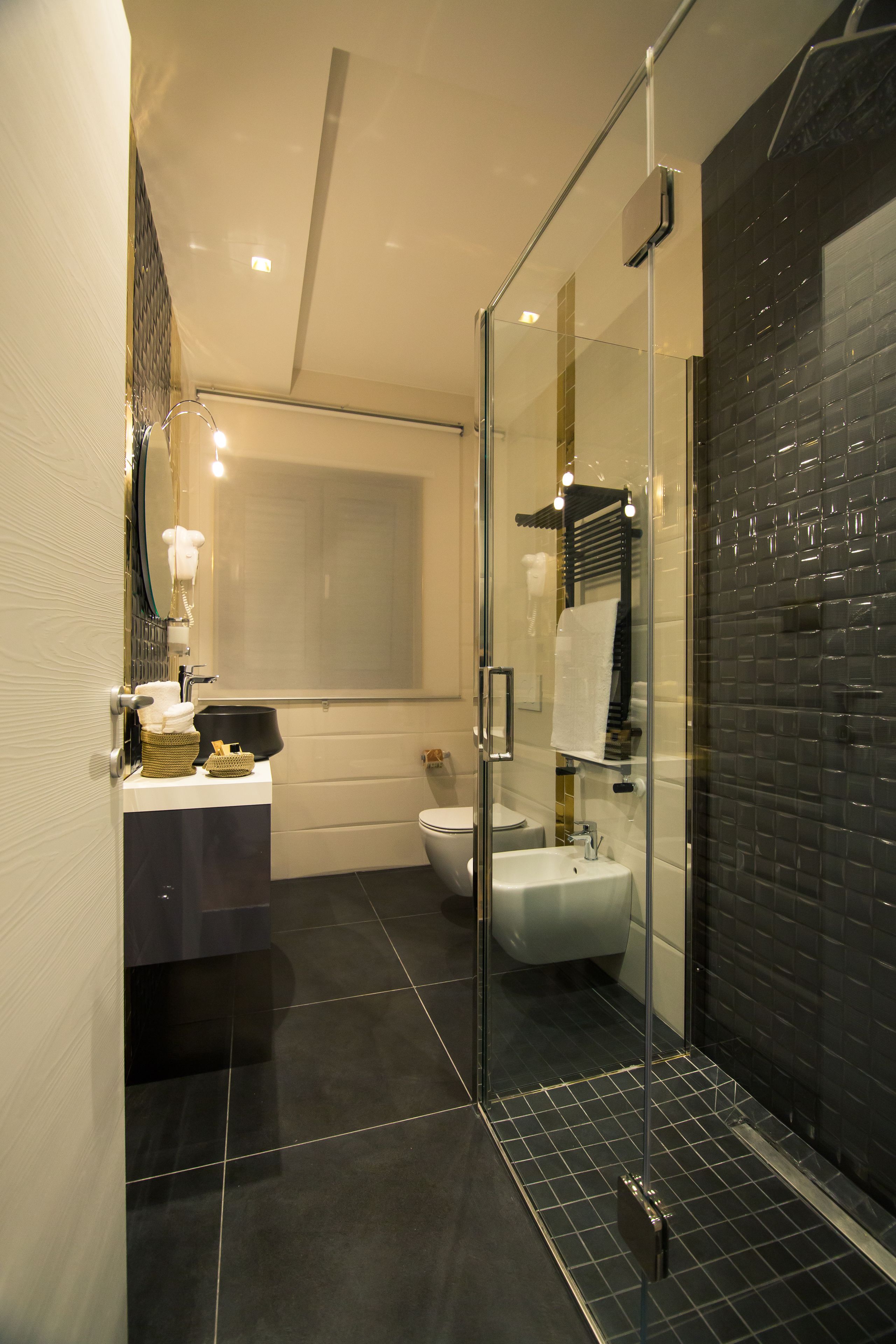 Un baño moderno con cabina de ducha de vidrio, un lavabo blanco y suelo de baldosas negras.