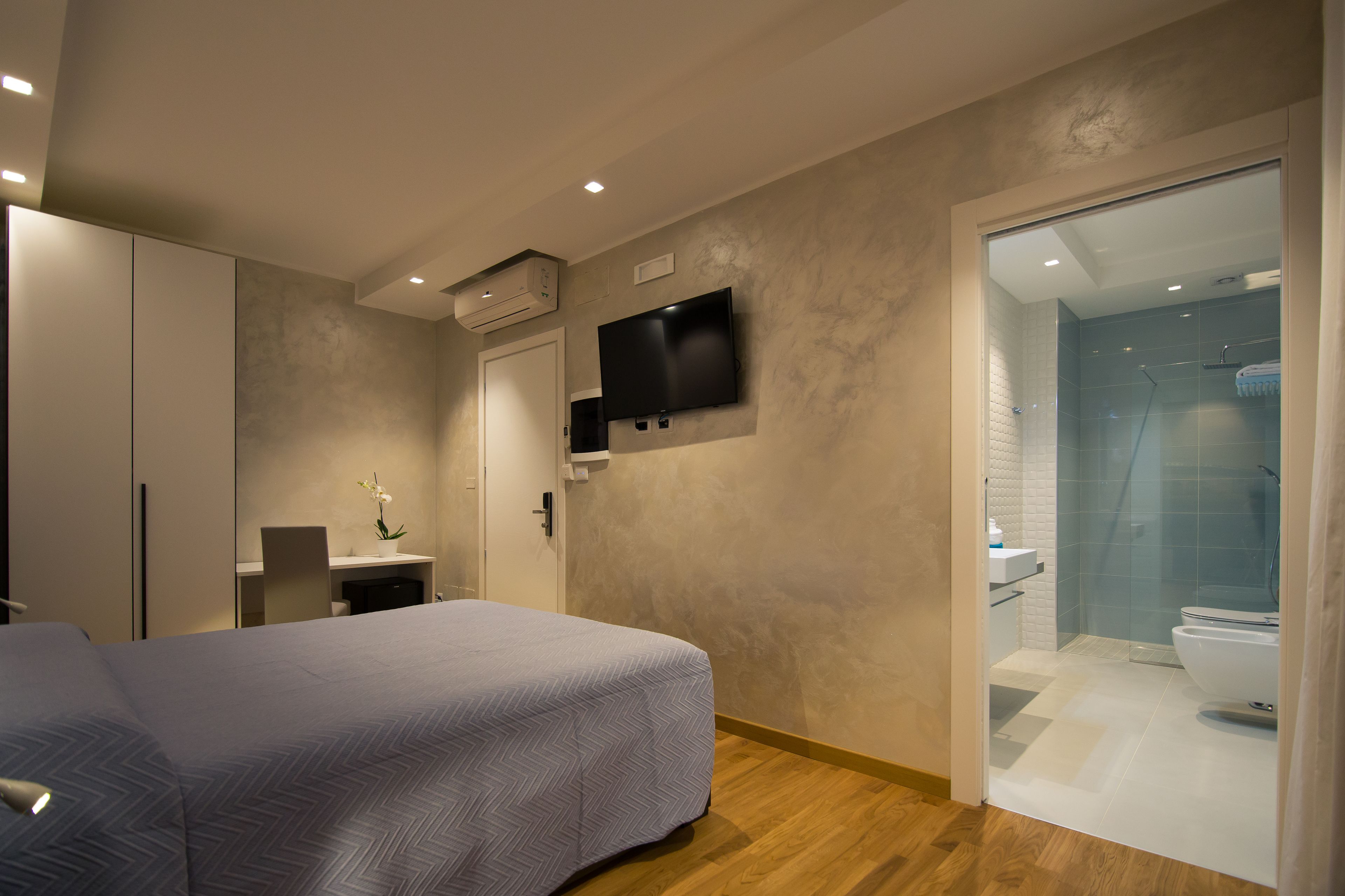 A bedroom with a bed, a desk, a TV, and a bathroom with a shower and toilet.