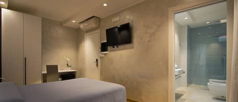 A bedroom with a bed, a desk, a TV, and a bathroom with a shower and toilet.