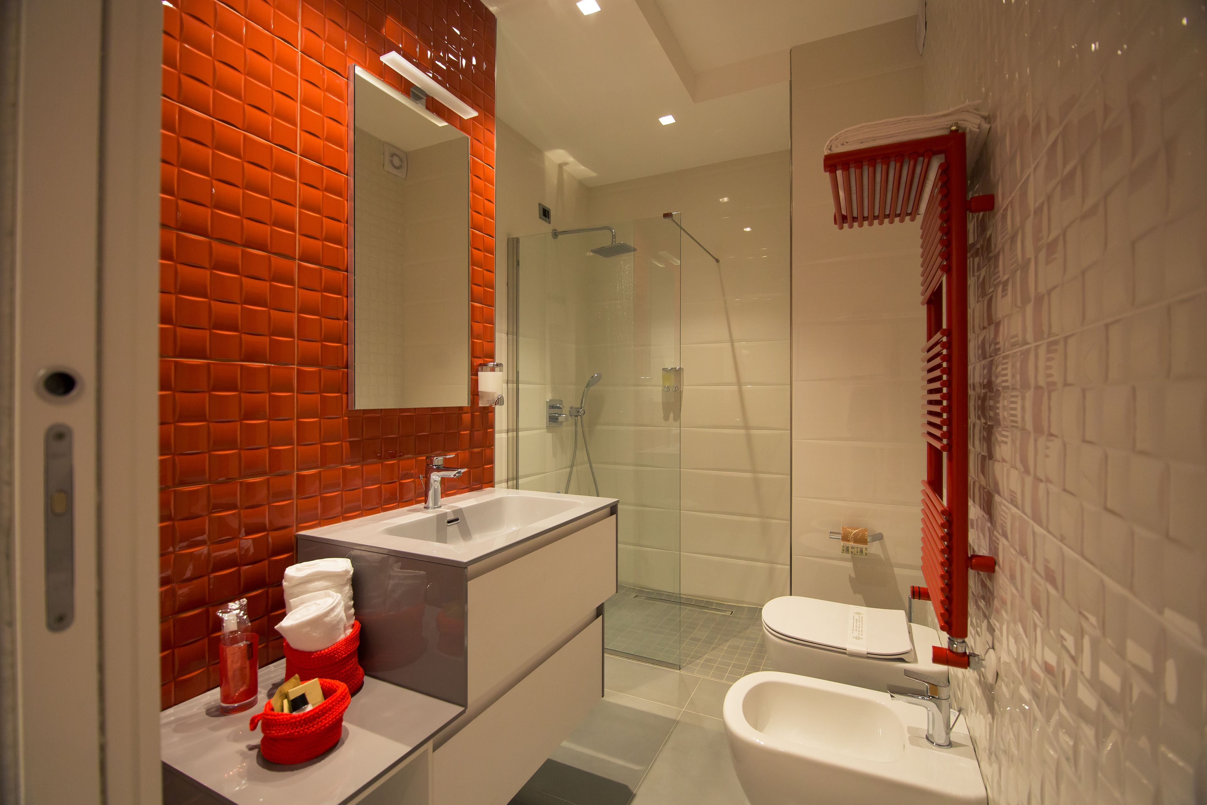 Un baño moderno con ducha de vidrio, lavabo blanco y toallero rojo.