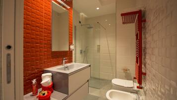 Un baño moderno con ducha de vidrio, lavabo blanco y toallero rojo.