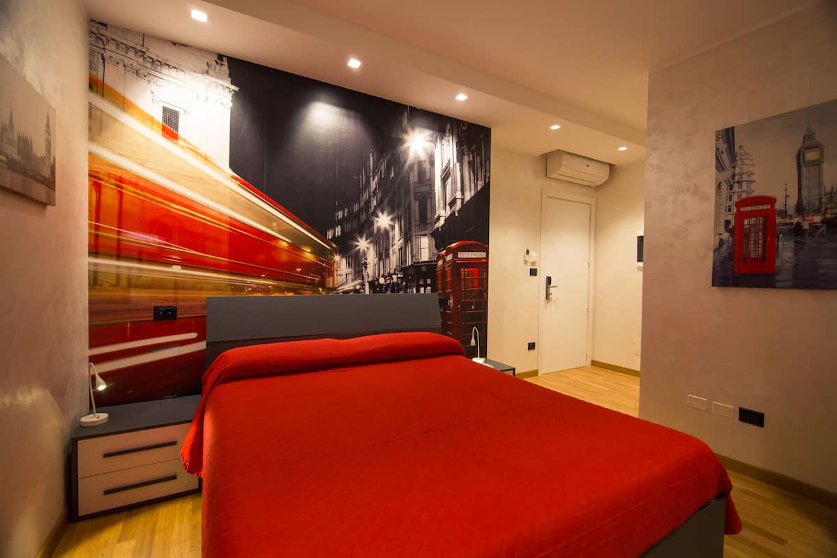 A modern bedroom with a large bed, a cityscape mural, a telephone booth, and a door.