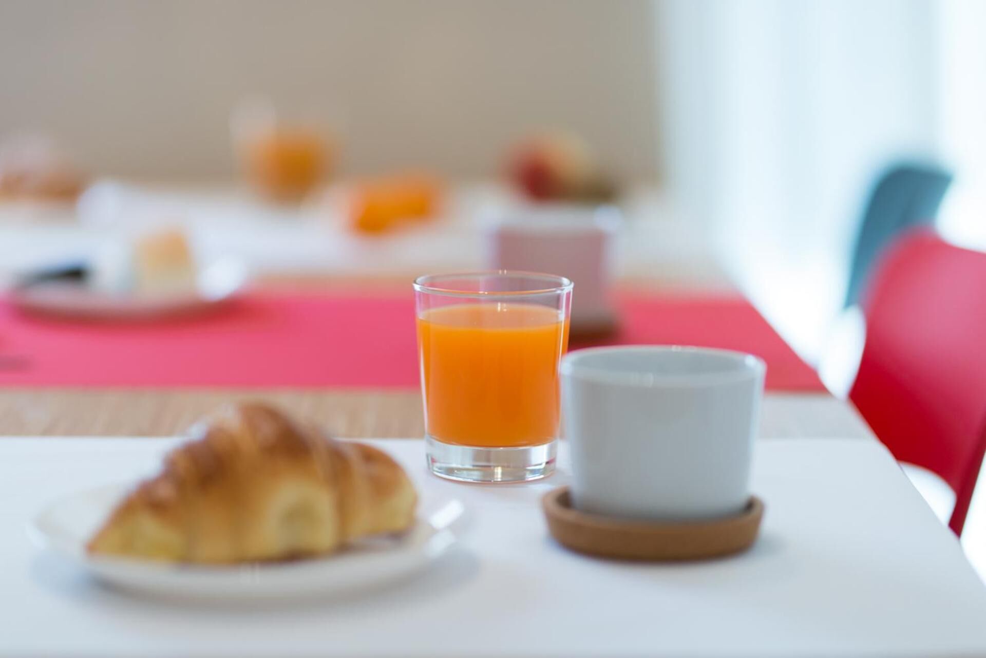 A breakfast setting with a croissant, a glass of orange juice, and a white cup on a table.