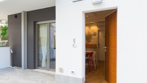 A modern building entrance with a sliding glass door, a wooden door, and a tiled patio area. - Le Mie Città (Pescara)