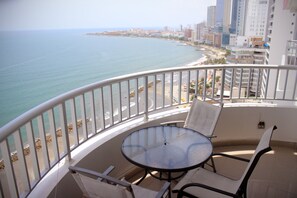 Un balcon avec une table ronde et des chaises, donnant sur une plage et offrant une vue sur la ville.