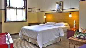 Una habitación de hotel con cama, ventana, teléfono montado en la pared y una planta.