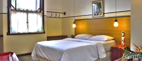 A hotel room with a bed, a window, a wall-mounted phone, and a plant.