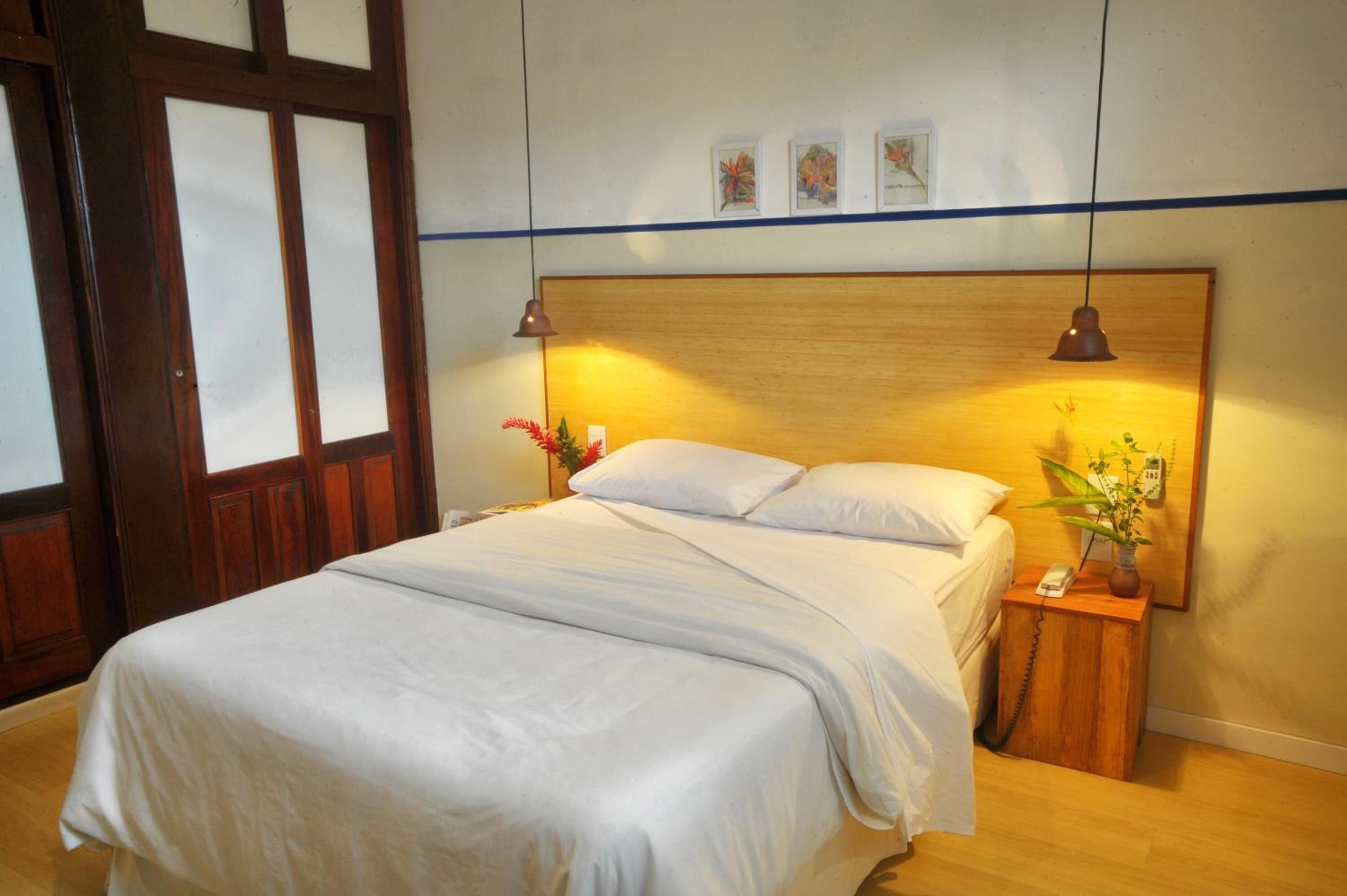 Een net opgemaakt bed met witte lakens, een houten hoofdbord en bedlampjes.