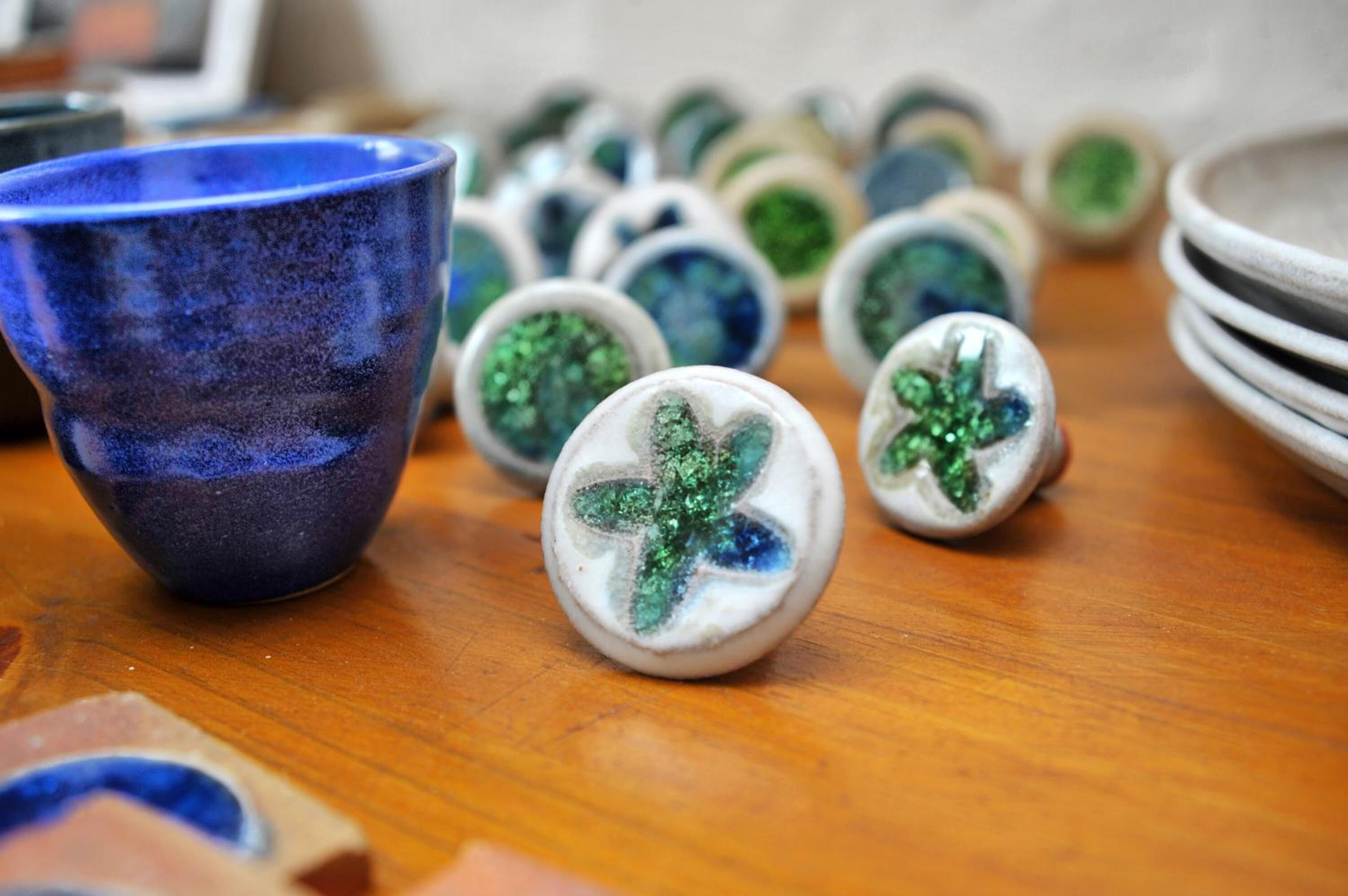 Una colección de objetos de cerámica sobre una mesa de madera, que incluye una taza de cerámica azul y varias piezas de cerámica blancas con diseños en verde y azul.