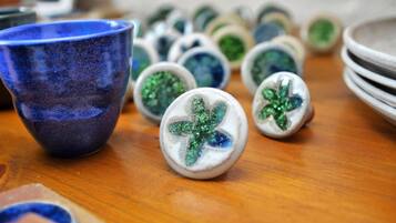 Una colección de objetos de cerámica sobre una mesa de madera, que incluye una taza de cerámica azul y varias piezas de cerámica blancas con diseños en verde y azul.