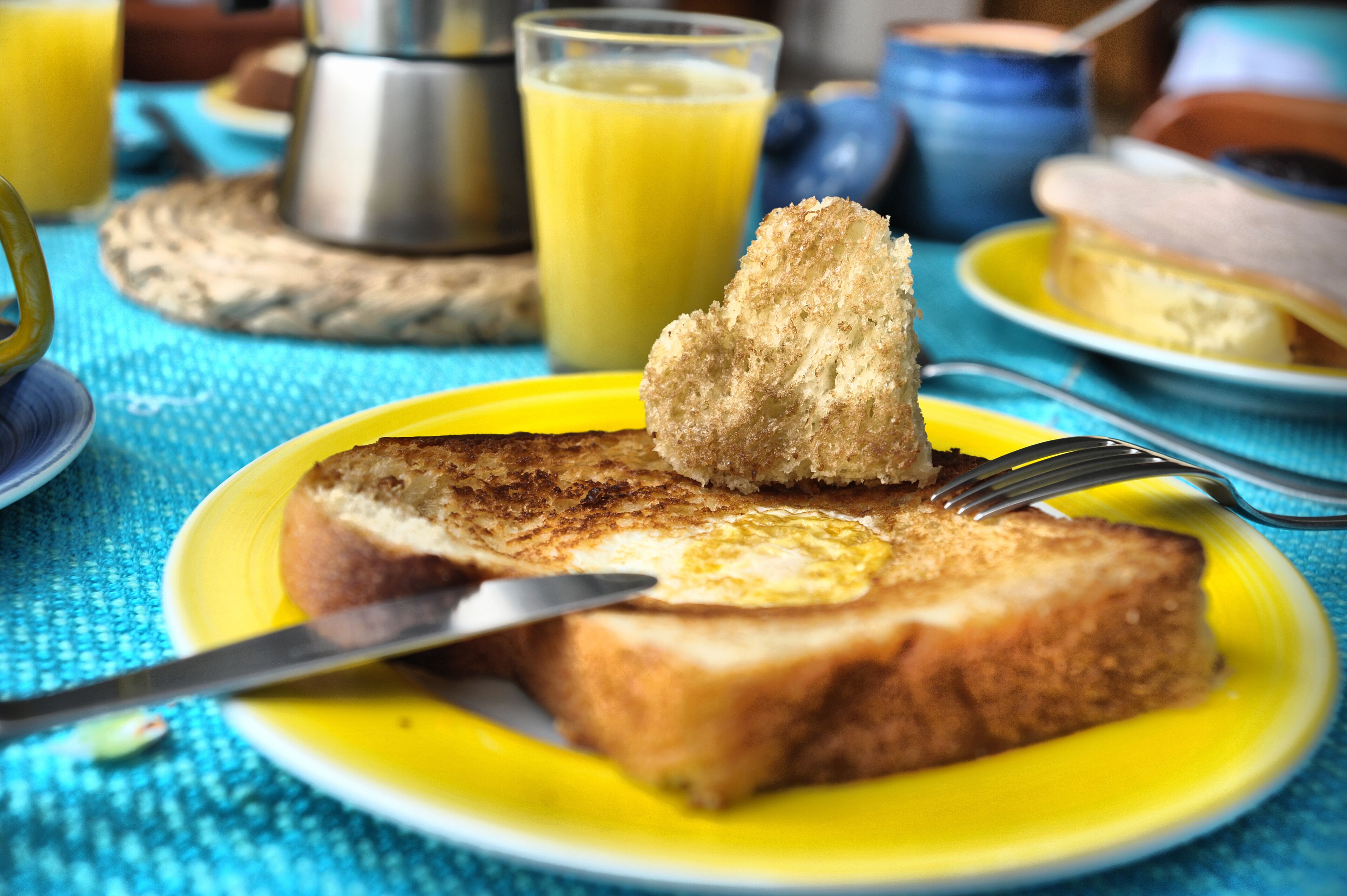 A breakfast setting with toast on a yellow plate, a fork, and a glass of orange juice.