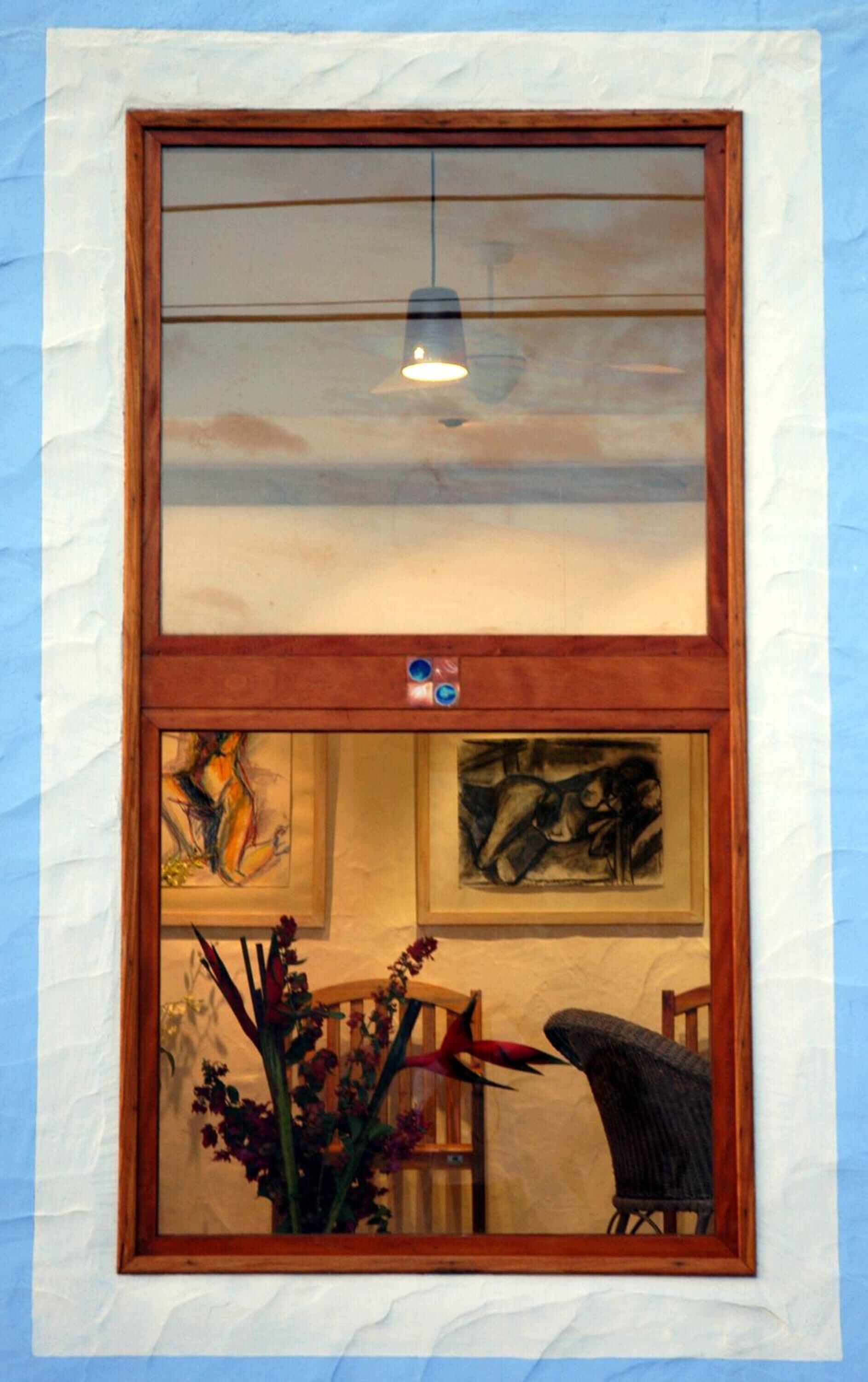 Uma janela com moldura de madeira, um lustre pendurado e duas obras de arte emolduradas abaixo.