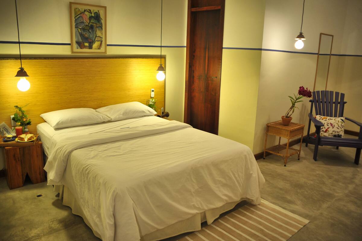 Un dormitorio ordenado con una cama grande, mesitas de noche, una silla y una puerta de madera.