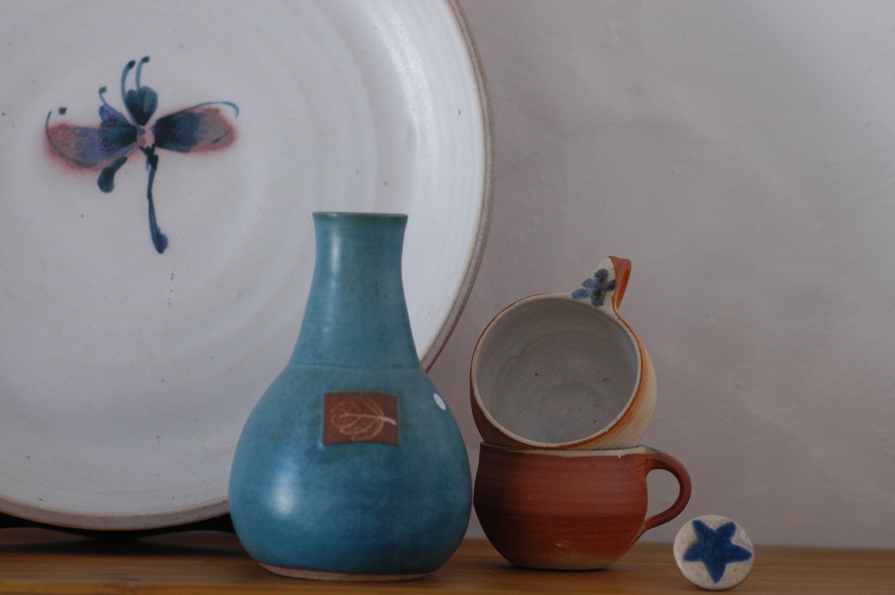 Un jarrón de cerámica, una taza y un plato con diseño de mariposa sobre una mesa.