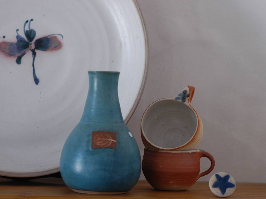 Un jarrón de cerámica, una taza y un plato con diseño de mariposa sobre una mesa.
