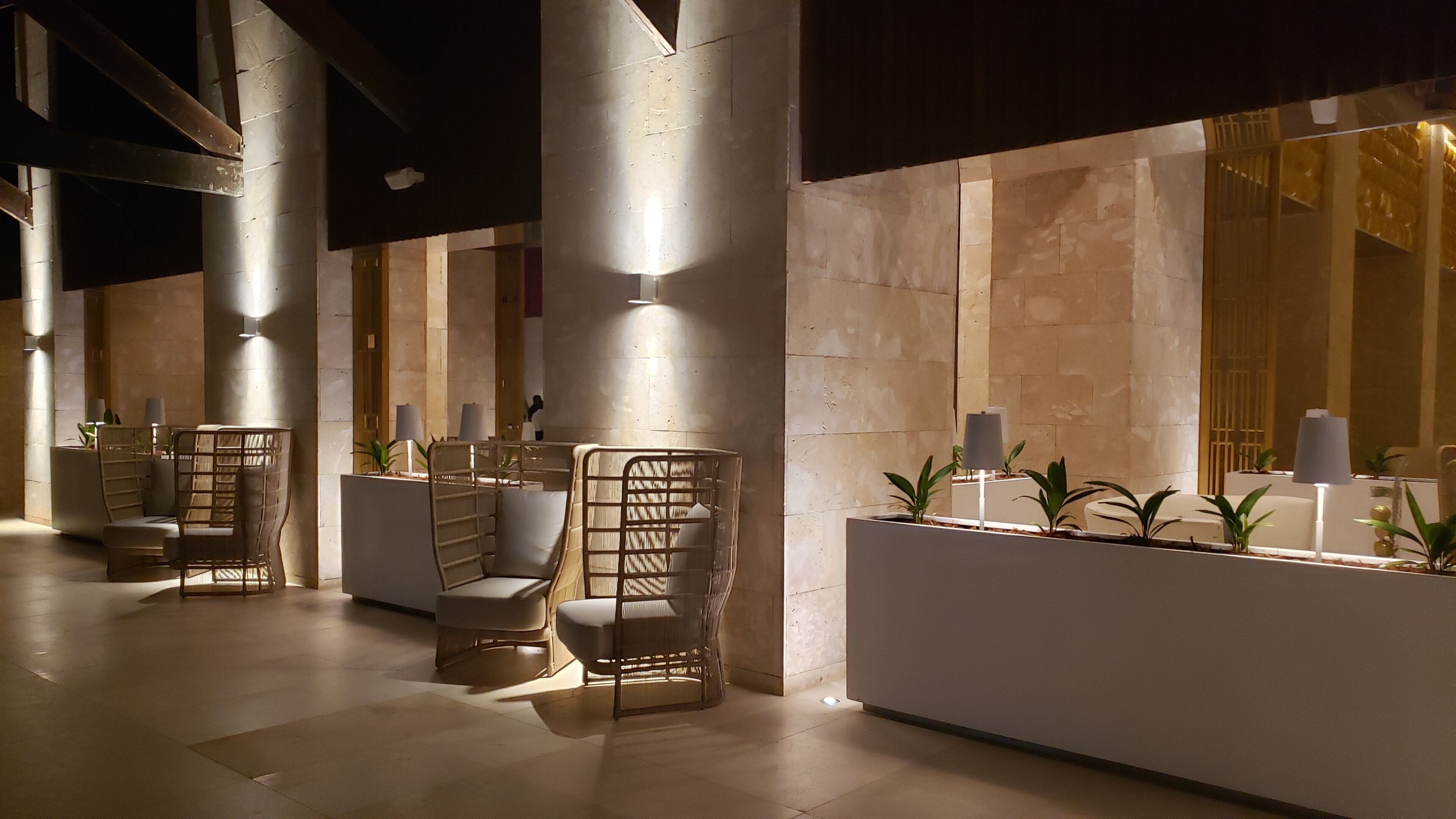 A modern lobby with high ceilings, large columns, and a reception desk with plants.