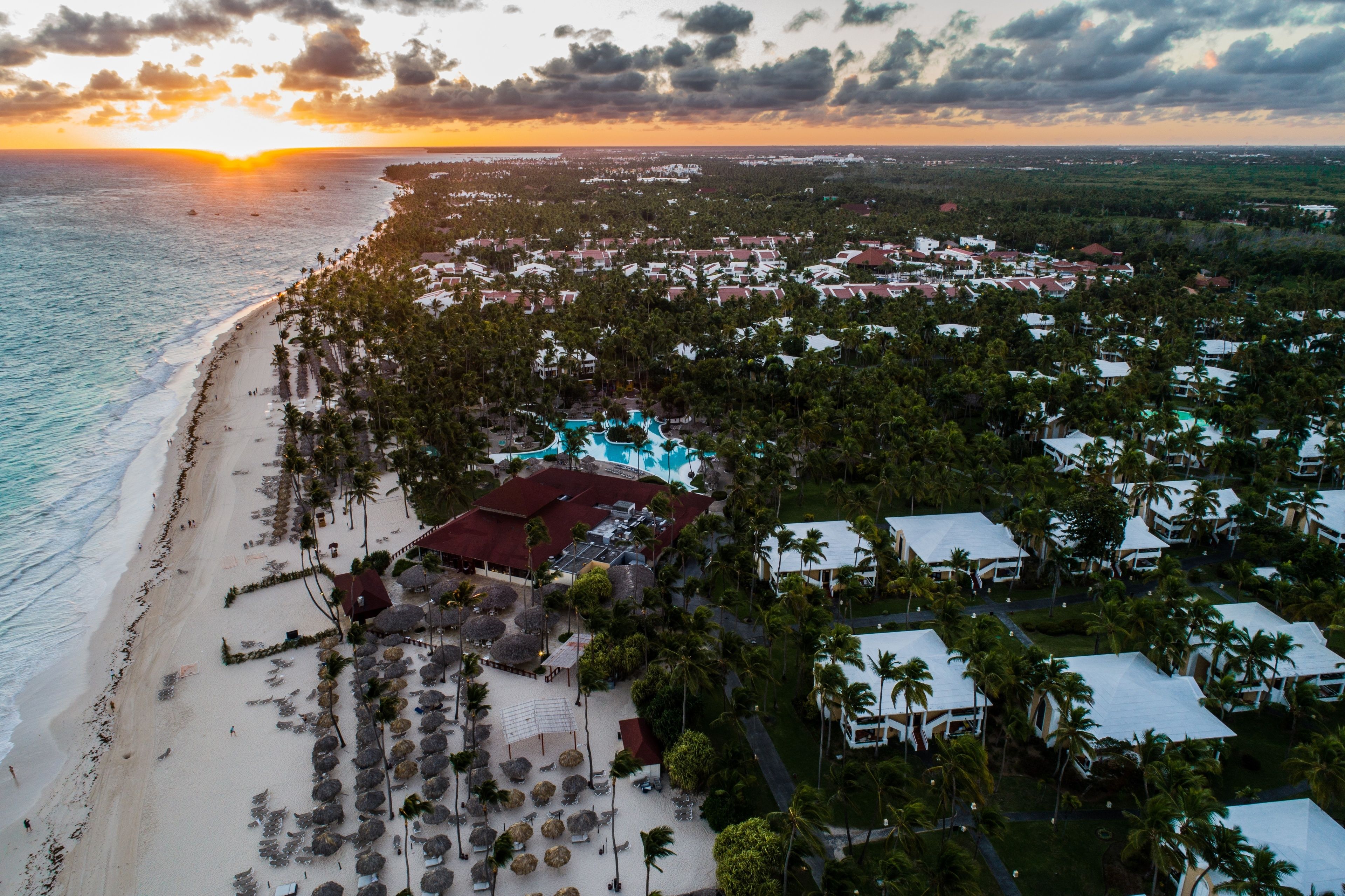 Vue aérienne d’un complexe hôtelier comprenant une plage, une piscine et un ensemble dense de villas.
