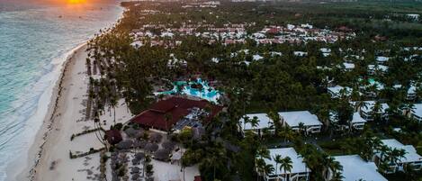 Vista aérea de um resort com praia, piscina e um conjunto denso de vilas.
