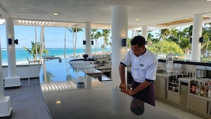 Eine Bar mit Blick auf Strand und Meer, einer Theke und einer Person, die Getränke zubereitet.
