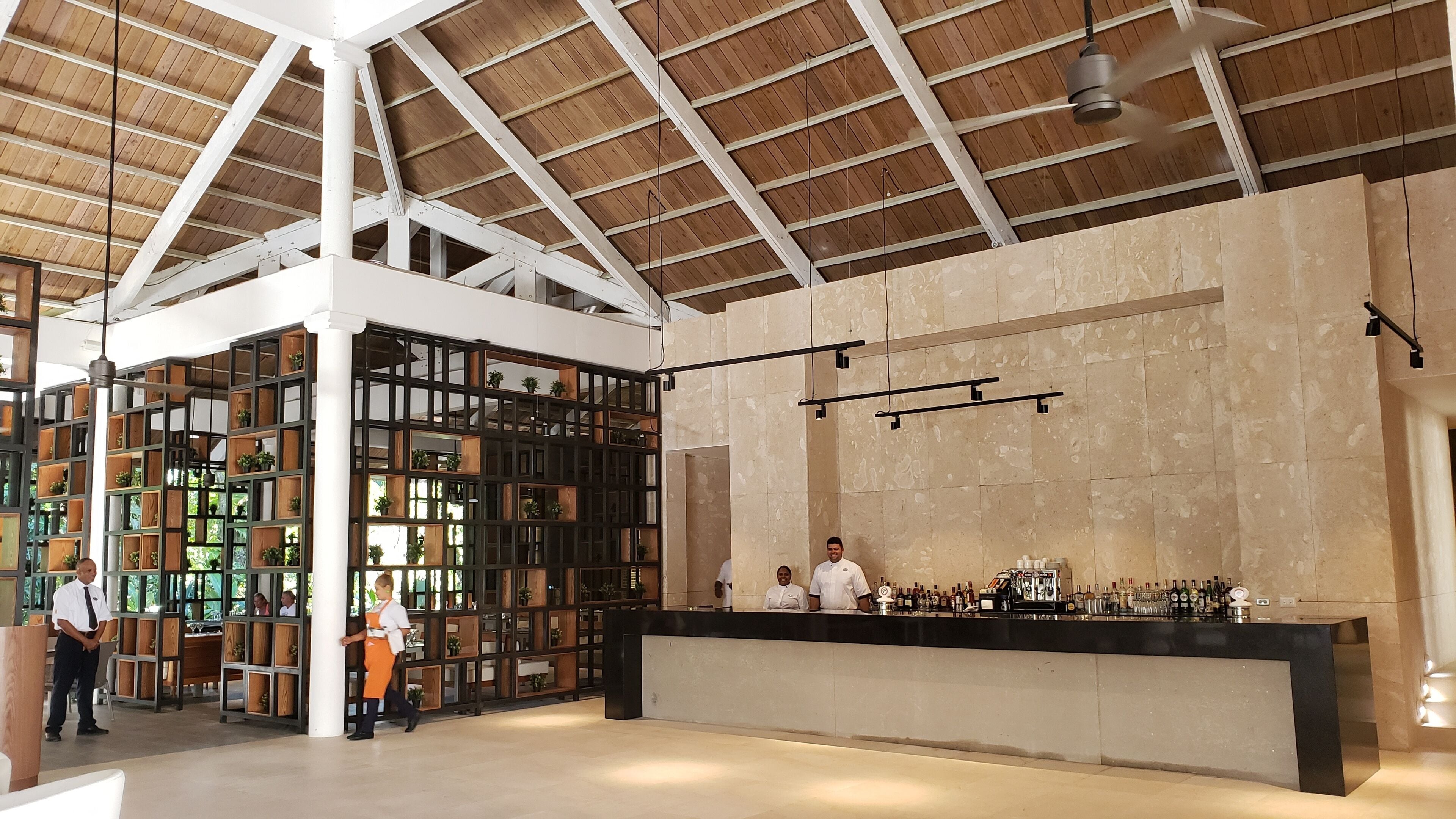 Un área de bar amplia con techo alto y vigas de madera, que presenta una barra con diferentes botellas y copas.
