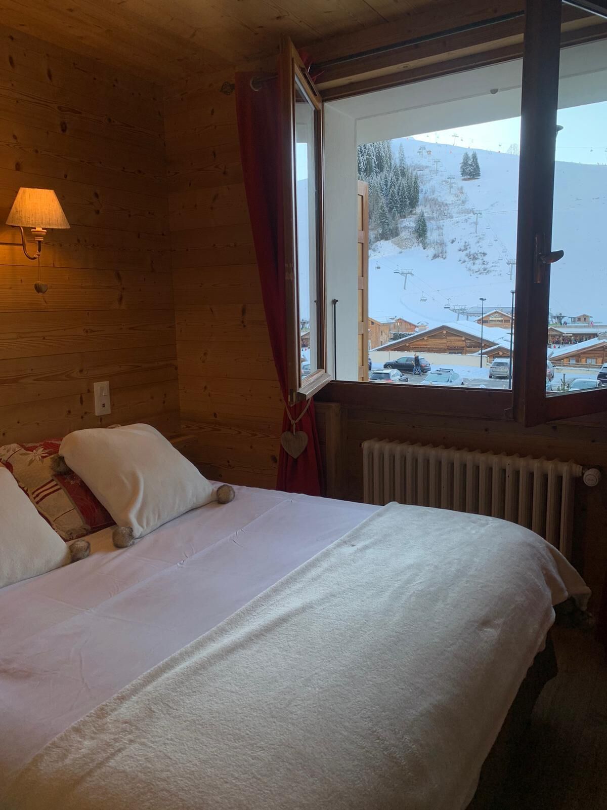 Ein Holzhüttenraum mit einem Bett, einem Fenster mit Blick auf eine verschneite Landschaft und einer Wandlampe.