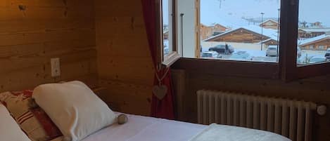 En stuga med träpanel, ett rum med en säng, ett fönster med utsikt över ett snötäckt landskap och en vägglampa.