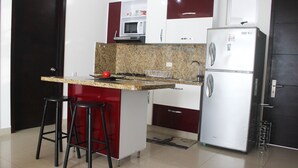 Uma cozinha compacta com bancada de granito, micro-ondas, geladeira e dois bancos altos.